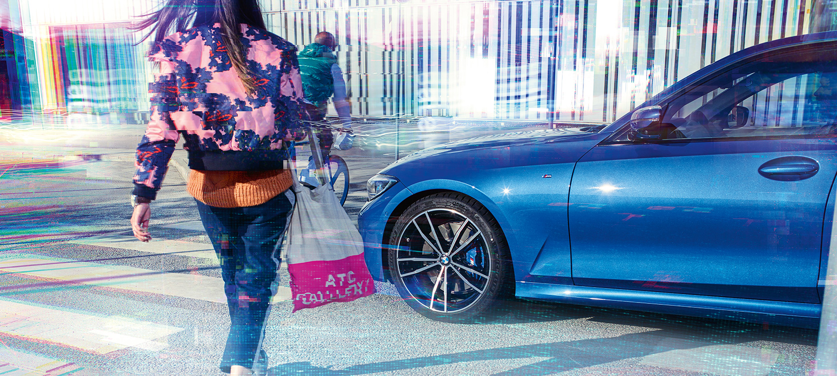 BMW 3 Series Saloon, three-quarter side shot. Three-quarter side shot of the BMW 3 Series Saloon on asphalt in front of an urban backround with passengers.
