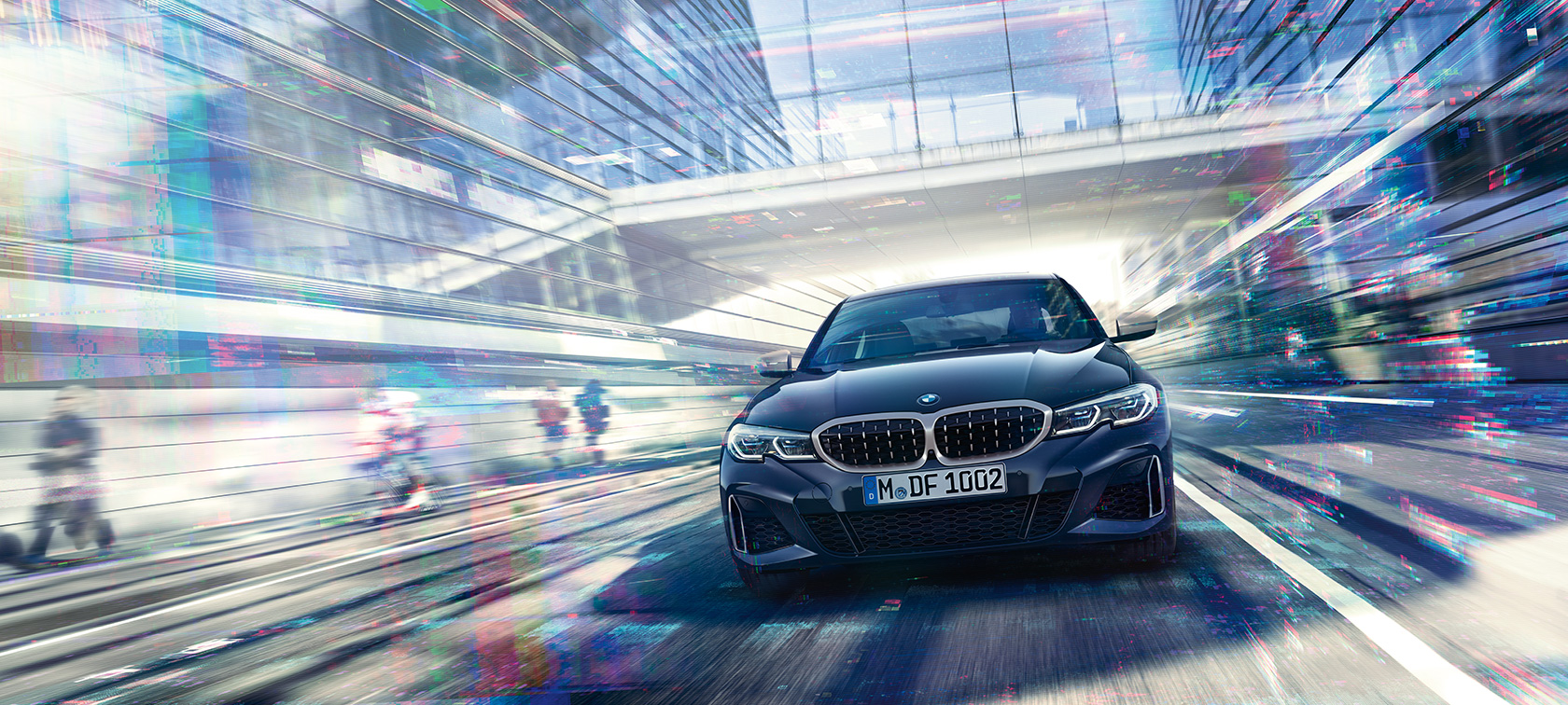 BMW 3 Series Saloon, frontal view BMW M340i xDrive. Frontal view of the driving BMW M340i xDrive Saloon between urban glass buildings.