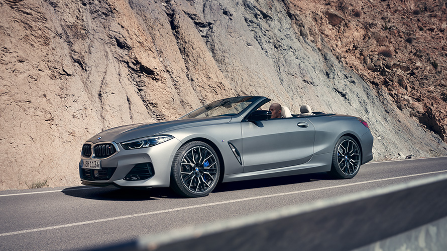 BMW 8 Series Convertible G14 LCI Facelift 2022 with open softtop driving along mountain wall BMW 8 Series Convertible G14 LCI Facelift 2022 BMW Individual Frozen Pure Grey metallic side view with open softtop driving along mountain wall