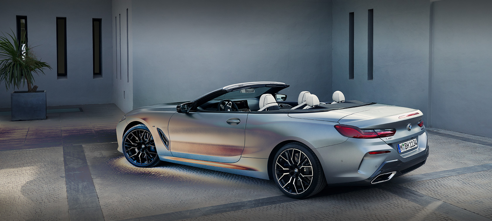 Man leaning against BMW 8 Series Convertible G14 LCI Facelift 2022 BMW Individual Frozen Pure Grey metallic side view standing in front of a building with male model
