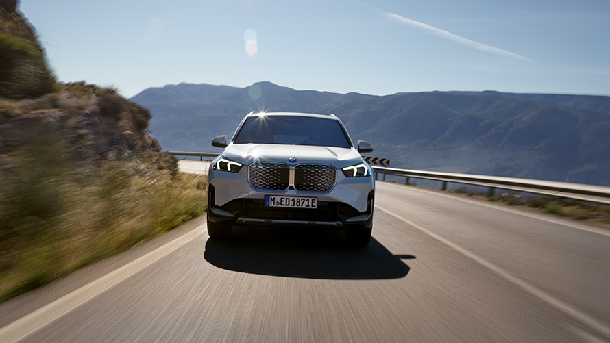 BMW iX1 U11 BEV 2022 front view BMW iX1 U11 BEV 2022 Mineral White metallic front view mountain road driving