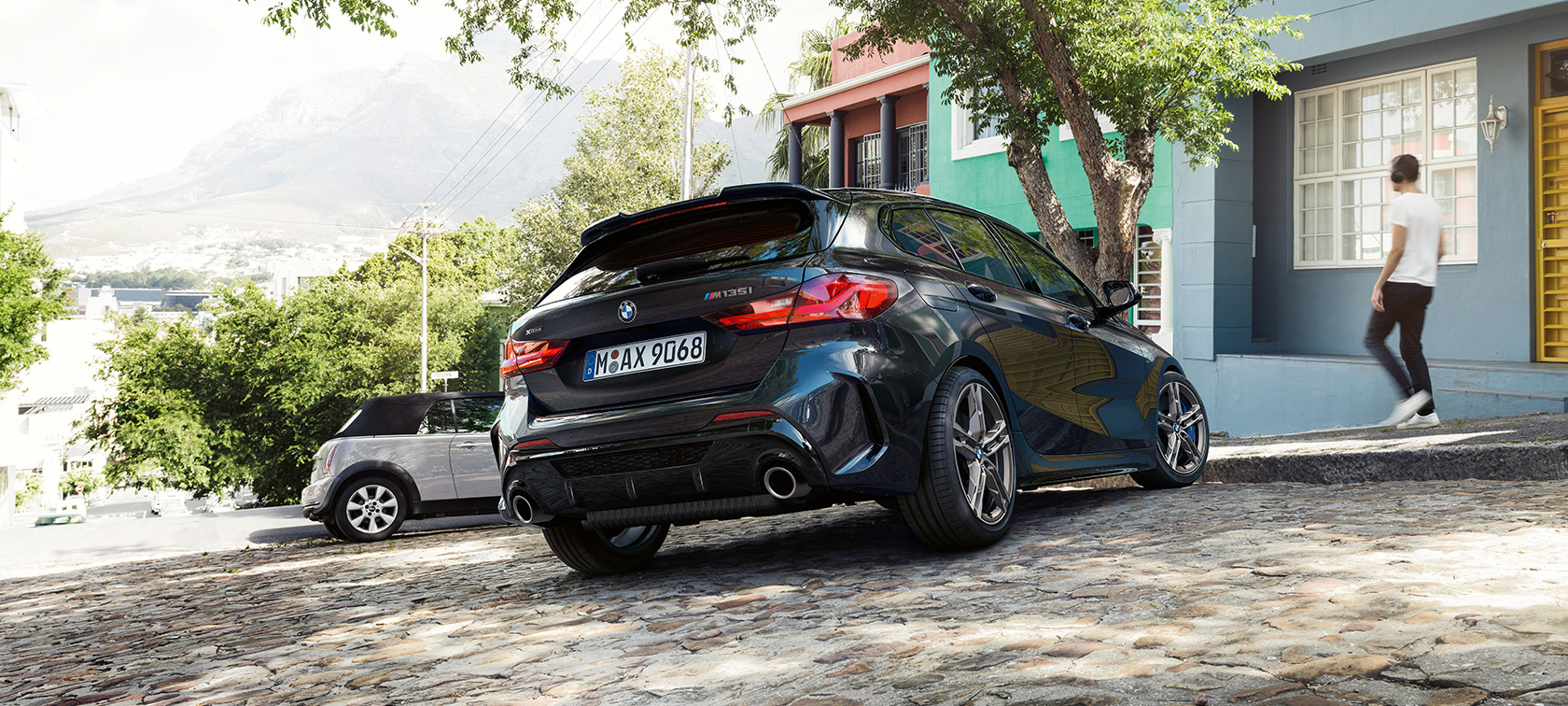 BMW M135i xDrive, three-quarter rear view. BMW M135i xDrive in Black Sapphire metallic, three-quarter rear view parking in front of a residential building.