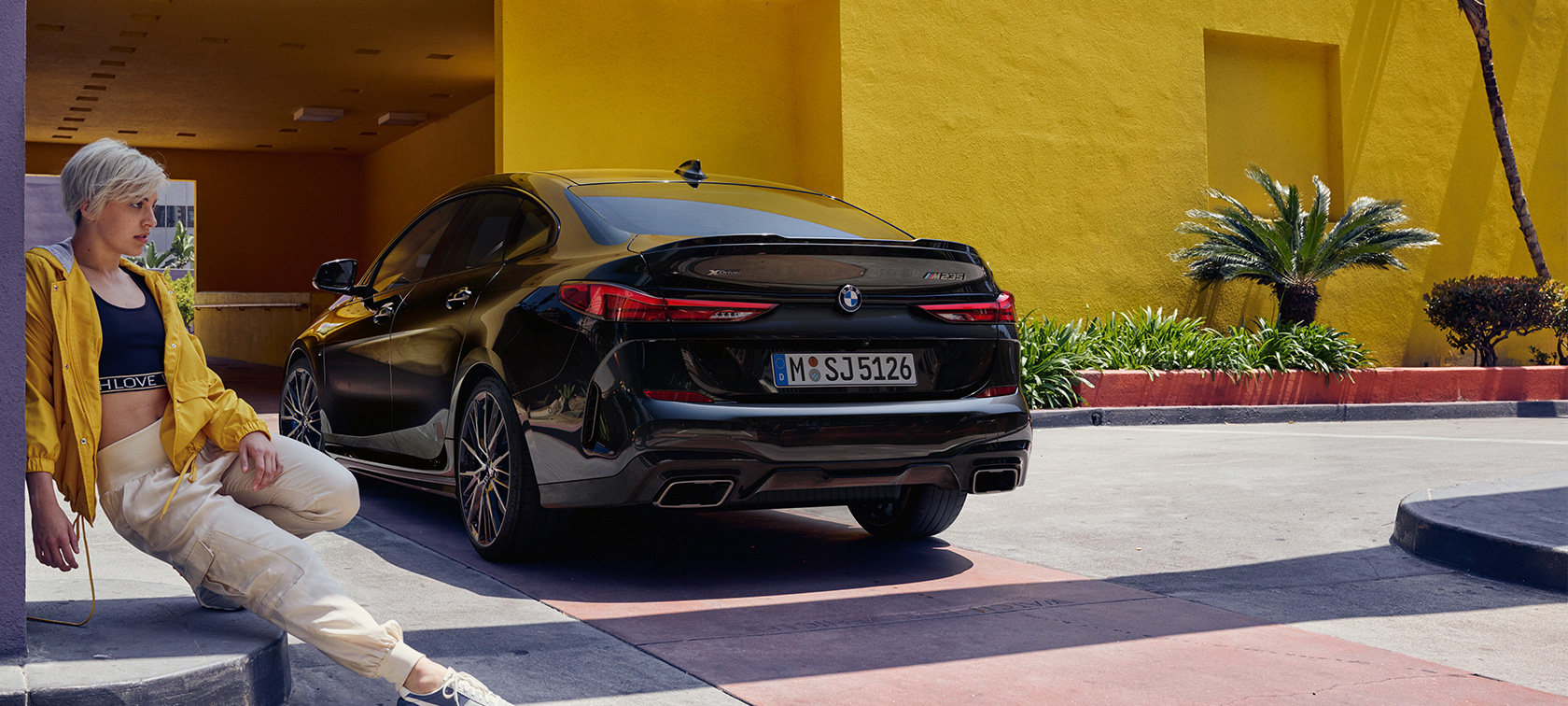 BMW M235i xDrive Gran Coupé three-quarter rear view BMW M235i xDrive Gran Coupé Black Sapphire metallic F44 three-quarter rear view with woman in the front