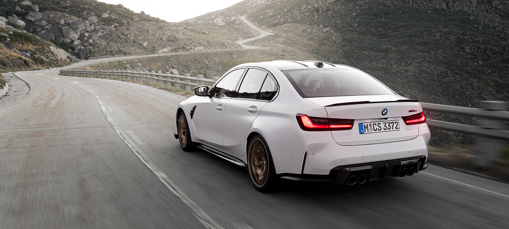 BMW M3 CS G80 three quarter rear view driving BMW M3 CS G80 three quarter rear view driving on the road in the mountains