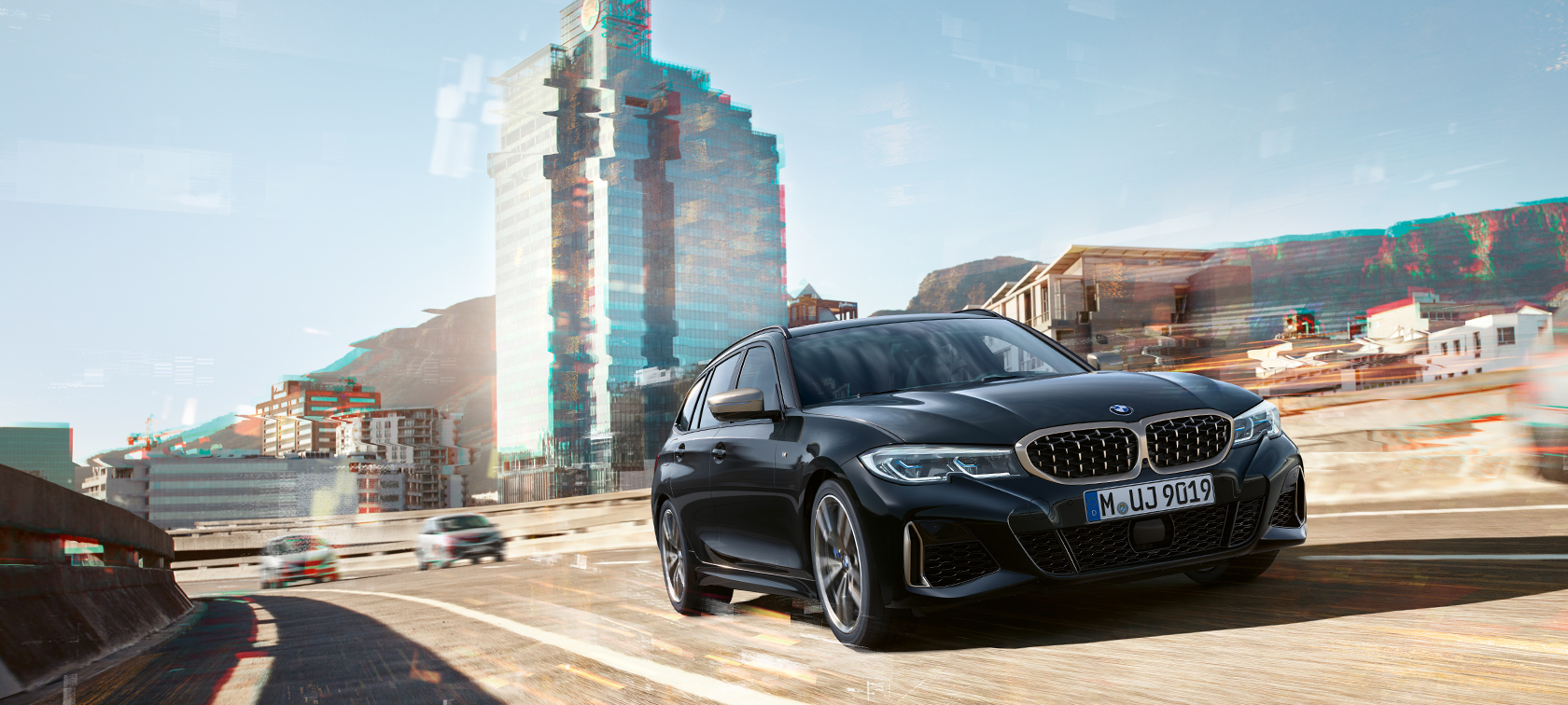 Three-quarter front shot driving in front of an urban backround BMW M340i xDrive Touring, Three-quarter front shot driving in front of an urban backround