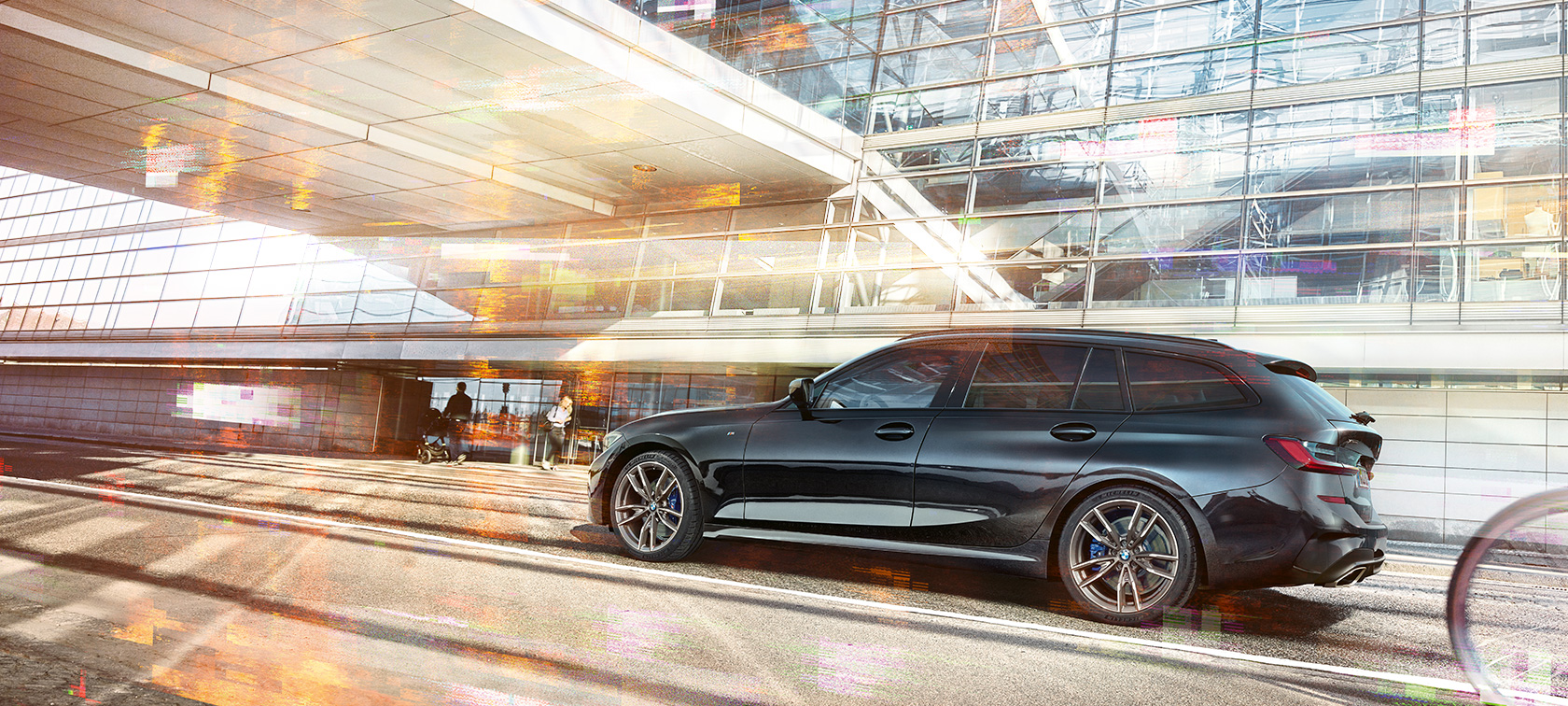 BMW M340i xDrive Touring, lateral driving shot BMW M340i xDrive Touring, lateral driving shot in front of an urban glass building