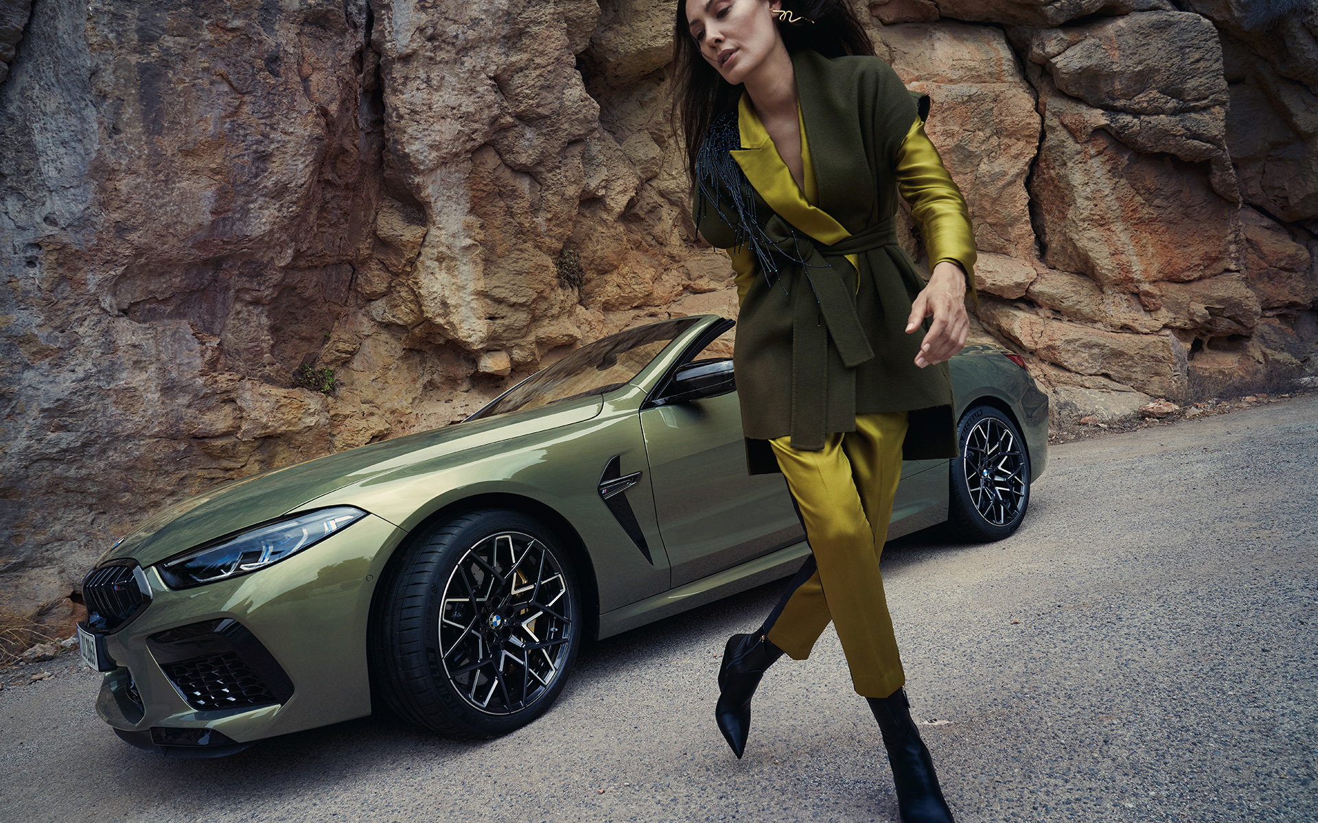 BMW M8 Competition Convertible F91 LCI 2022 three-quarter front view standing in stony terrain BMW M8 Competition Convertible F91 LCI Facelift 2022 BMW Individual Brass metallic three-quarter front view standing in stony terrain with female model