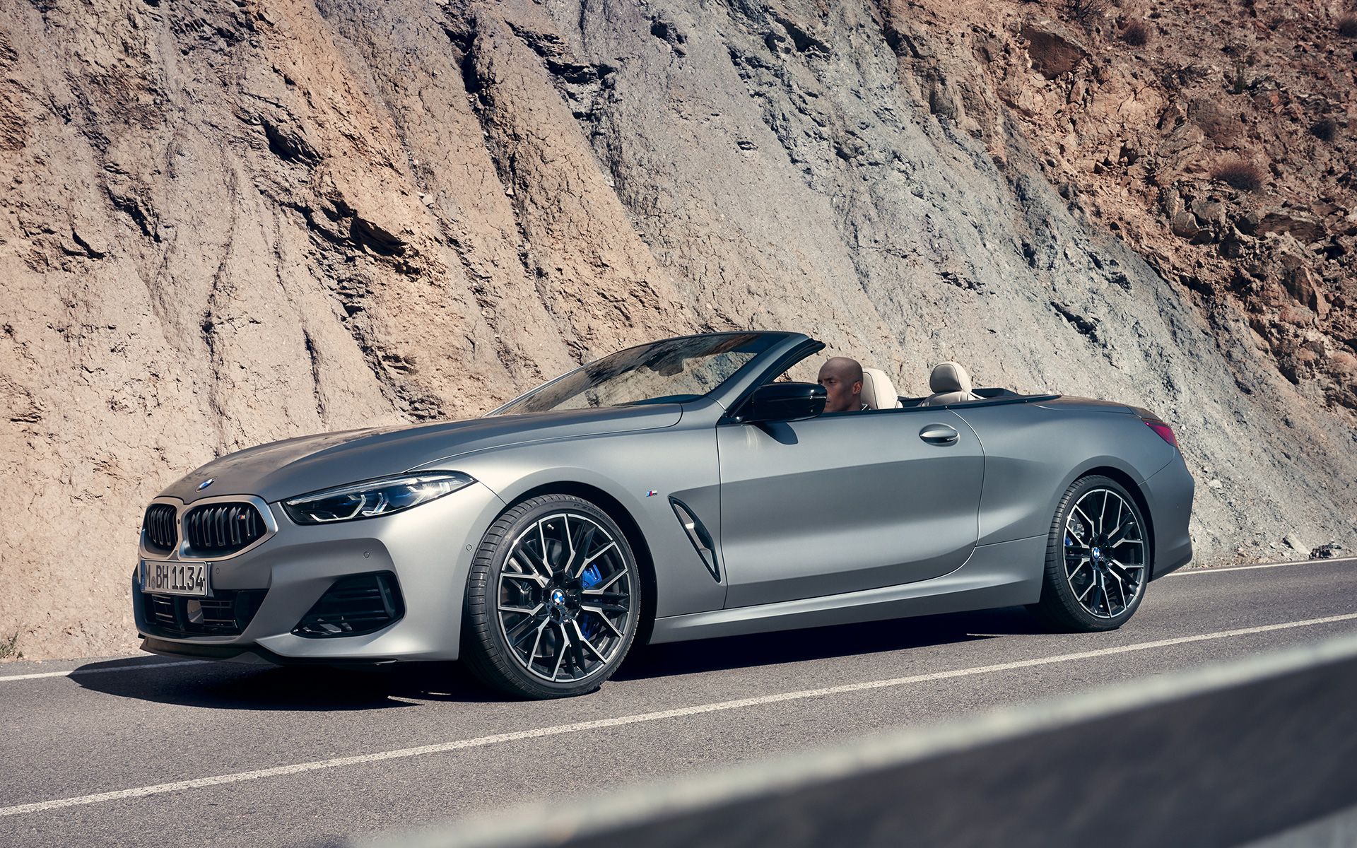 Three quarter front view BMW M850i xDrive Convertible G14 LCI Facelift 2022 BMW M850i xDrive Convertible G14 LCI Facelift 2022 BMW Individual Frozen Pure Grey metallic three quarter front view driving in front of cliff face