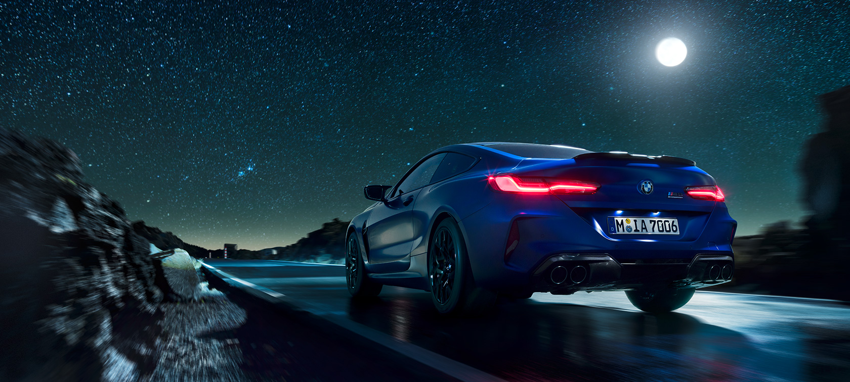 BMW M8 Competition Coupé, rear view. BMW M8 Competition Coupé, rear view, driving at night with full moon.