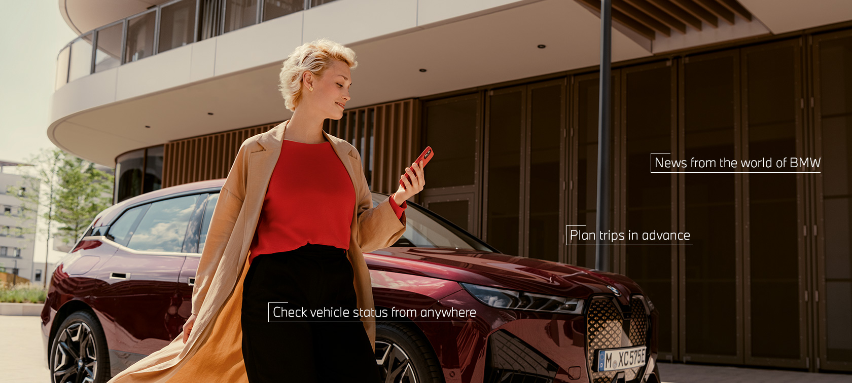 Woman in front of BWW iX uses My BMW app on smartphone Woman in front of BWW iX uses My BMW app on smartphone