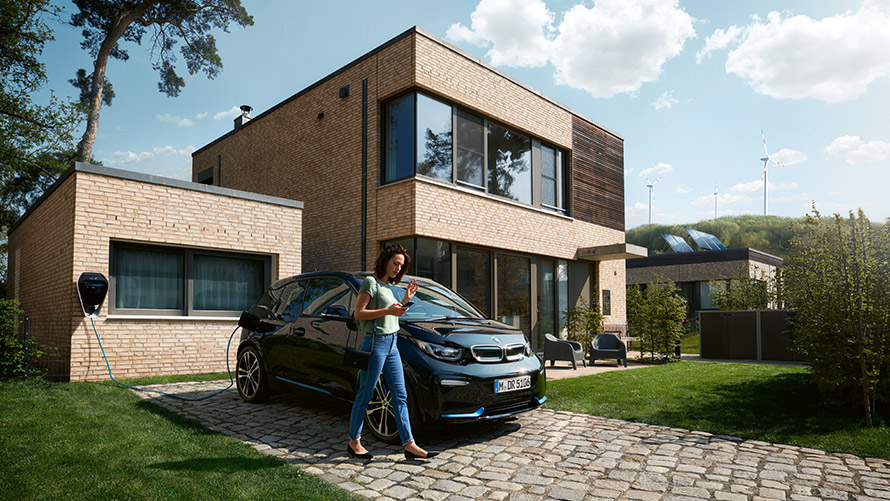 Digital Charging Service Woman walks outside in front of her BMW i3 and uses Digital Charging Service on smartphone